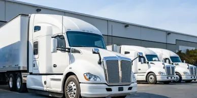 Three white semi-trucks parked outside a building.