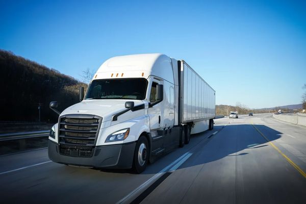 A white semi-truck driving on a highway under a clear blue sky.
