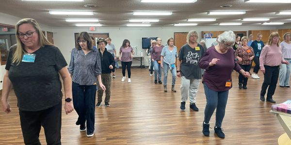 Group of adults participating in a line dancing class indoors.