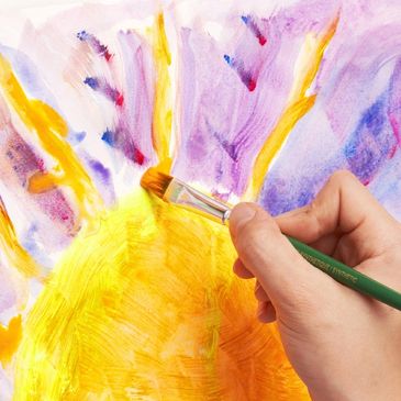 Close-up of a hand painting a sun on canvas.