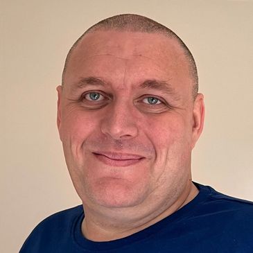 Smiling man with blue eyes and a shaved head wearing a navy blue shirt.
