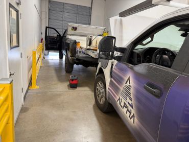 Two trucks inside a garage with tools on the floor.