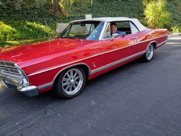A man smiling in a red classic convertible car with a white roof.
