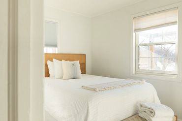 Bright, minimalistic bedroom with white bedding and wooden headboard.
