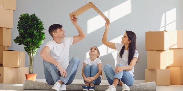 Family sitting on carpet with cardboard boxes, holding a frame above their heads.