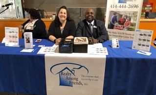 Two representatives smiling at a Realty Among Friends booth with informational displays.