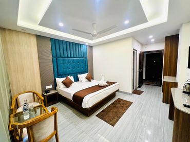 Modern hotel room with a large bed, blue headboard, and wooden furniture.