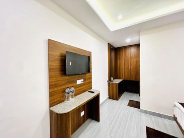 Minimalist hotel room corner with TV, wooden furniture, and water bottles.