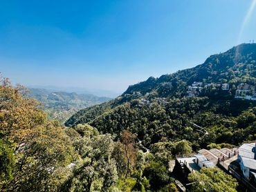 Scenic mountain landscape with houses nestled among lush green trees under a clear blue sky.