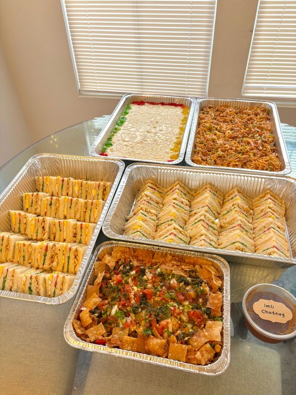 A variety of sandwiches and Indian dishes served in foil trays on a glass table.