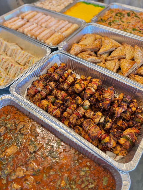 A variety of delicious dishes in aluminum trays, including grilled skewers and sandwiches.