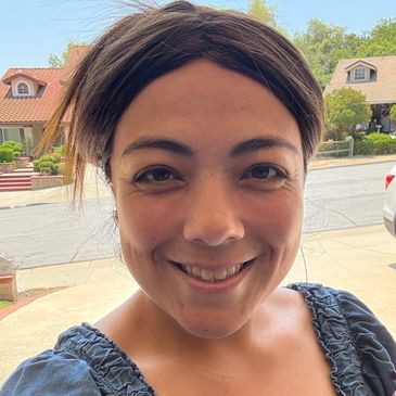 A woman smiling outdoors with houses in the background.