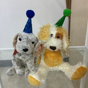 Two plush dogs wearing colorful party hats sitting side by side.