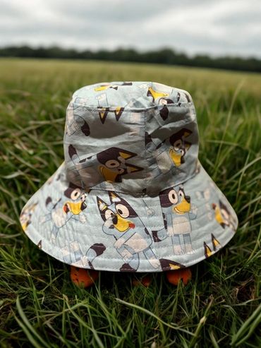 A bucket hat with cartoon dog designs placed on grass outdoors.