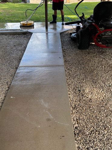 Man power washing a patio near a lawn mower and gravel.
