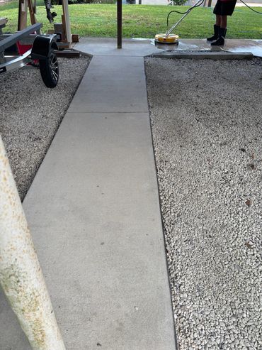Person pressure washing a concrete surface outdoors with gravel on the side.