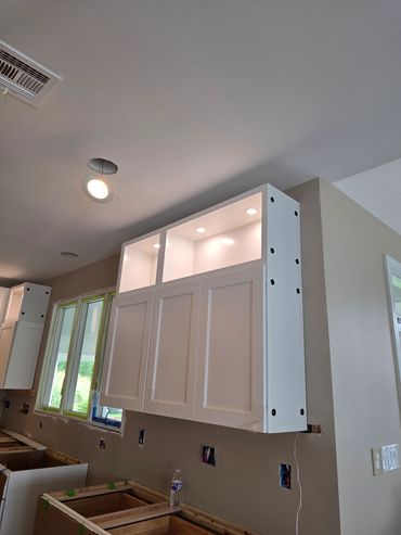 Kitchen cabinets being installed with lighting and unfinished electrical work.