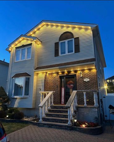 Two-story house with warm exterior lights and a welcoming entrance at dusk.