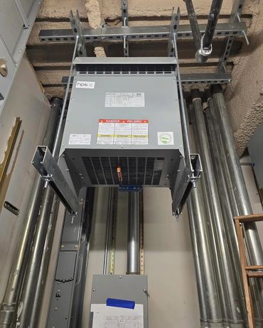 Industrial electrical panel with warning labels and metal conduit pipes.