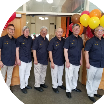 Six men in matching navy shirts and white pants stand in a line, smiling indoors.