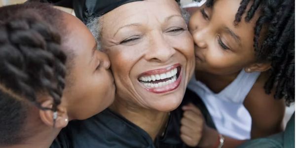 Two children kissing an elderly woman on her cheeks, smiling.