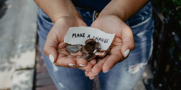 Person holding coins and a note saying 'Make a Change'.