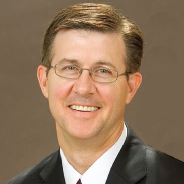 Smiling man in glasses and suit against plain background.