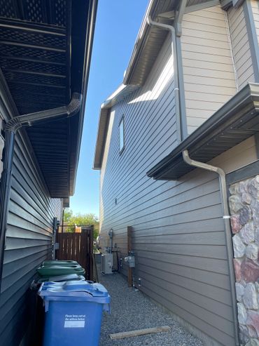 Alley between two houses with trash bins and clear blue sky.