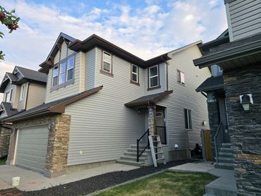 Modern two-story suburban house with beige siding and stone accents under a partly cloudy sky.