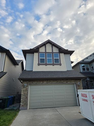 Modern two-story house with a double garage and stone facade under a partly cloudy sky.