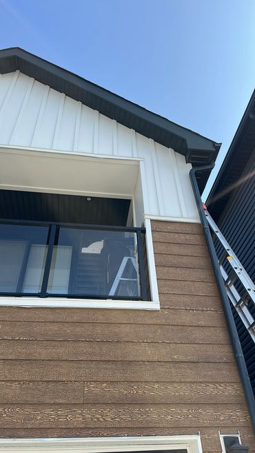 Person on ladder working on balcony of modern house under clear blue sky.
