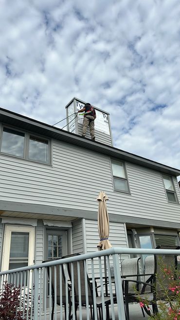 Worker installing siding on rooftop structure under cloudy sky.