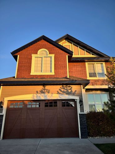Sunlit suburban house with wooden garage door and decorative windows.