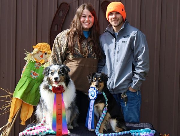 Two people with their prize-winning dogs wearing ribbons, posing happily.