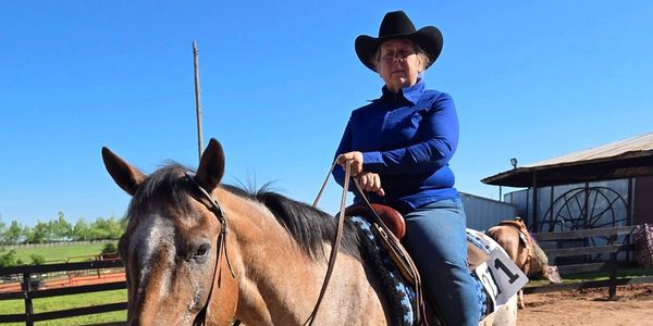 A woman in a cowboy hat riding a horse on a sunny day.