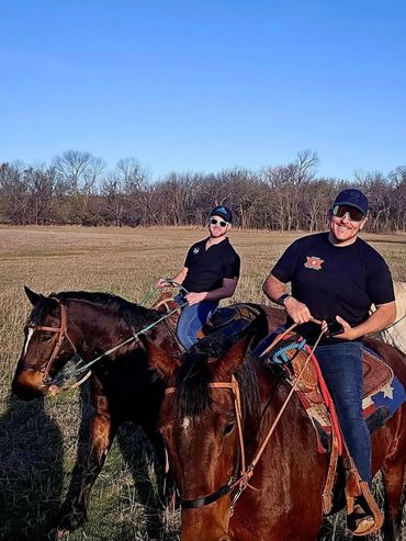 Two men smiling while horseback riding in a sunny field.