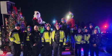 Police officers and Santa Claus posing by a Christmas tree at night.