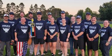 Police team posing outdoors with a trophy and softball equipment.