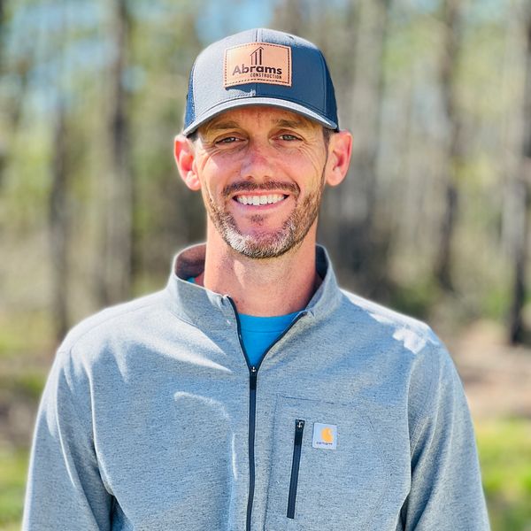 Man wearing a cap and a gray jacket smiling outdoors.