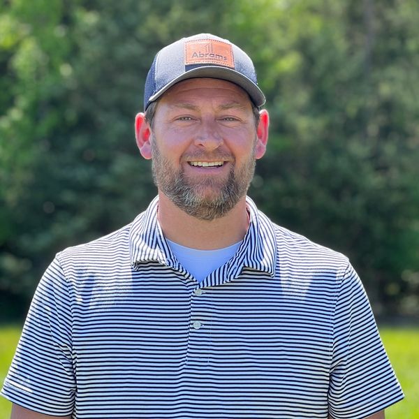 Smiling man in a striped polo and baseball cap outdoors.