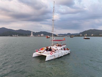 Golden Merry catamaran with guests on deck, floating in a harbor with a scenic city backdrop
