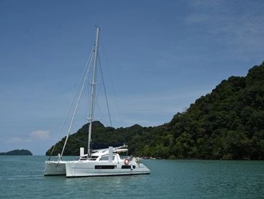 White sailing catamaran Kawanada anchored in turquoise waters near a lush green island