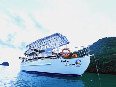 Puteri Zarra anchored in calm waters near a lush green island, with lifebuoy on deck