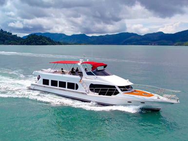 Sea Whale yacht with red canopy cruising through turquoise waters, surrounded by lush green islands