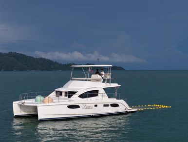 Two people seated on Victoria catamaran flybridge, with an island backdrop.