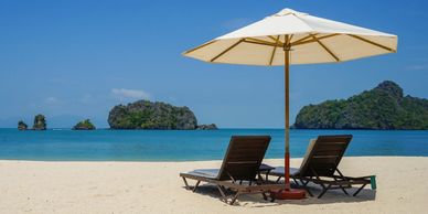 Two beach loungers under an umbrella facing the sea with island views in the background