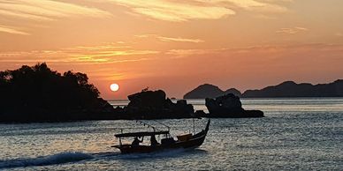 Small wooden boat sailing at sunset with island silhouettes in the background