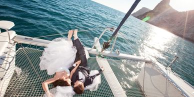 Bride and groom lying on a yacht netting over the sea, with sunlight reflecting on the water