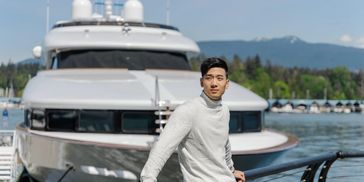 Asian man posing by a luxury yacht at a marina