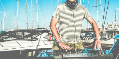 DJ playing music on a yacht with marina and sailboats in the background